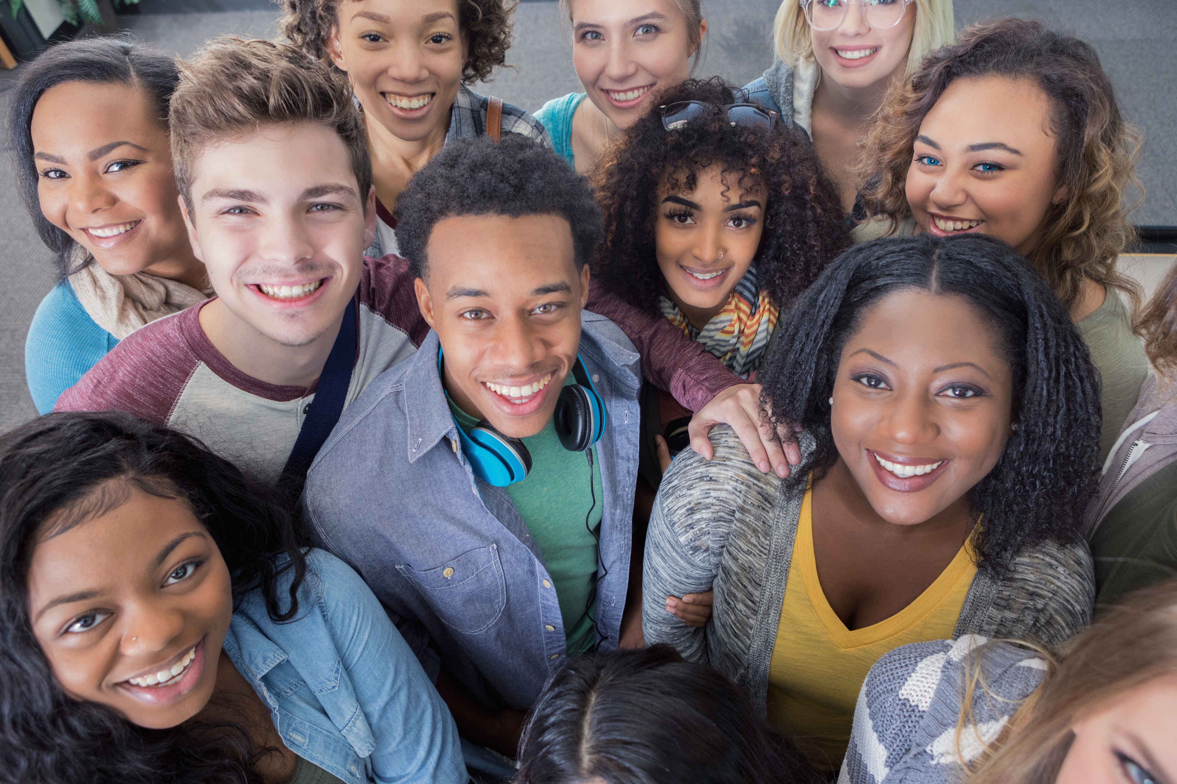 A large group of cheerful diverse young adults looking up and smiling at the camera. The group includes male and female African American, Hispanic and Caucasian ethnicities.